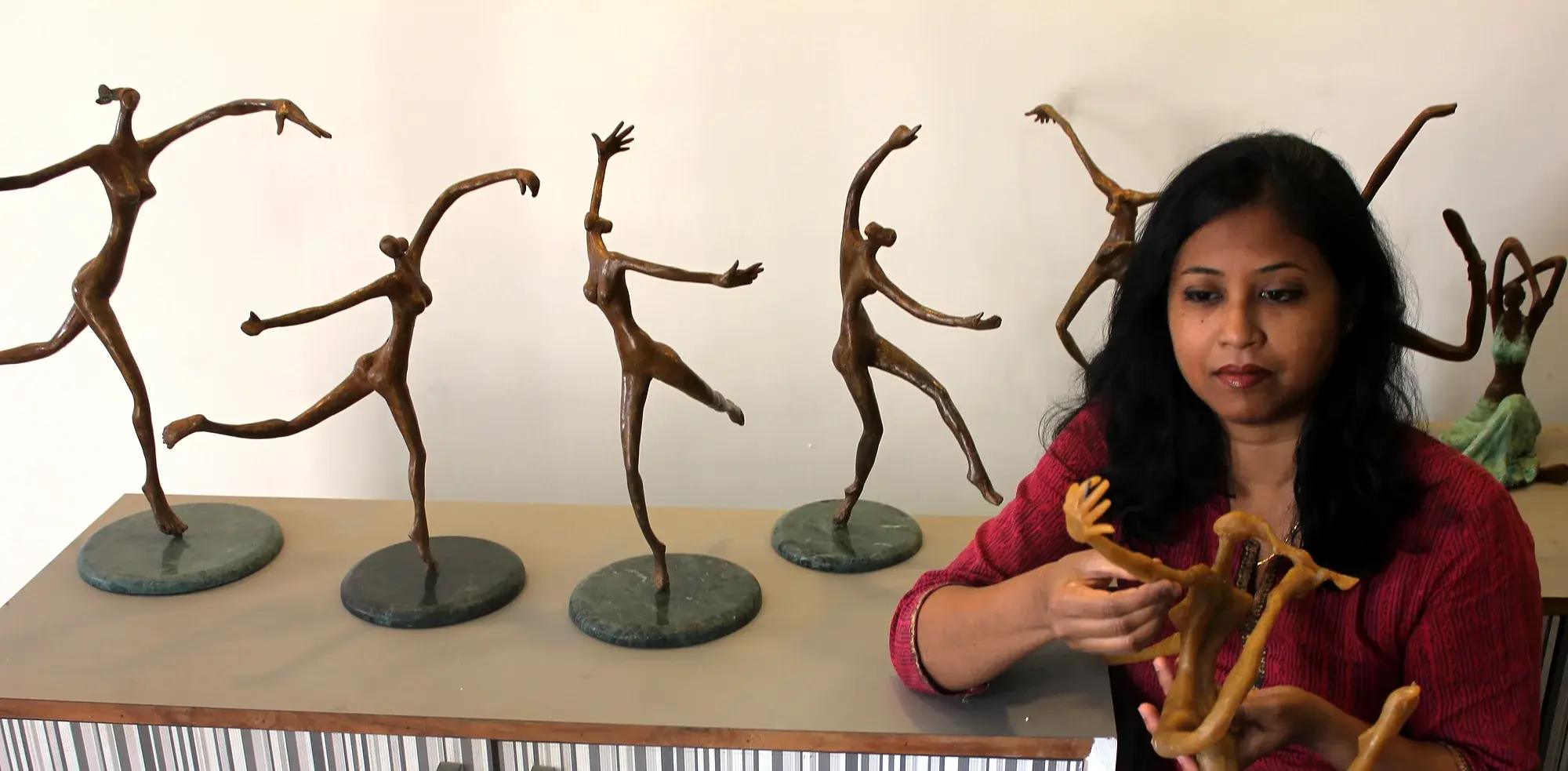 The artist in her studio with a row of bronze dancer maquettes on marble bases