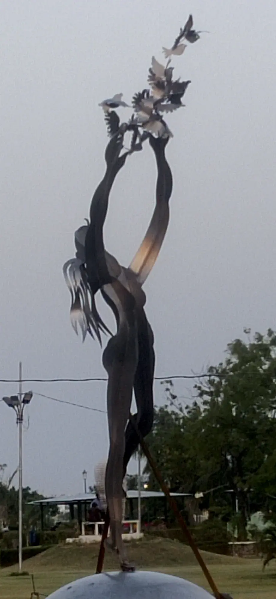 Freedom — a monumental stainless-steel figure releasing birds from open hands, installed outdoors against an evening sky