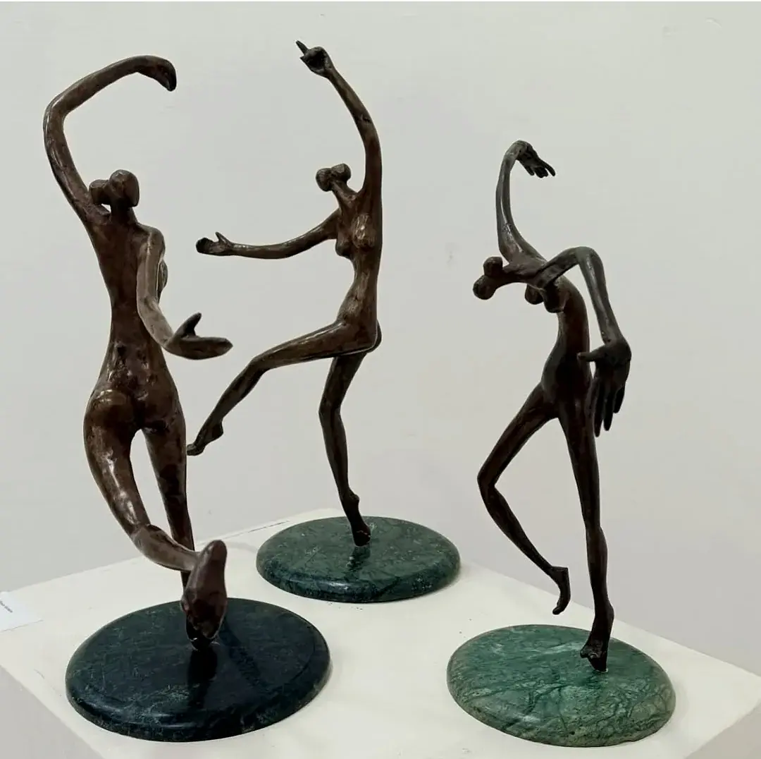 Three bronze nude dancing figures in mid-motion, each on a round green-marble base