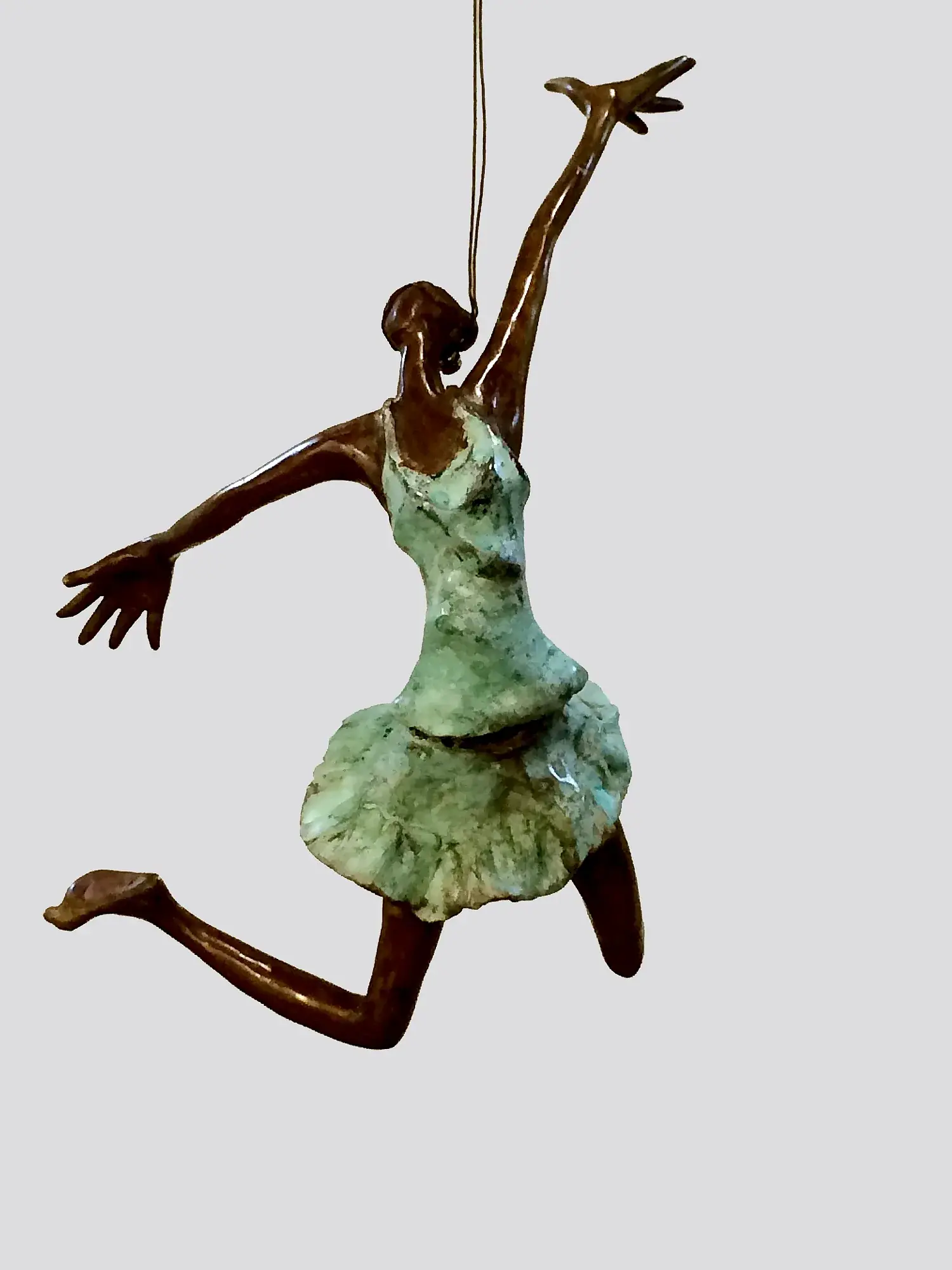A bronze dancer figure suspended by wire, mint-green dress, captured mid-leap