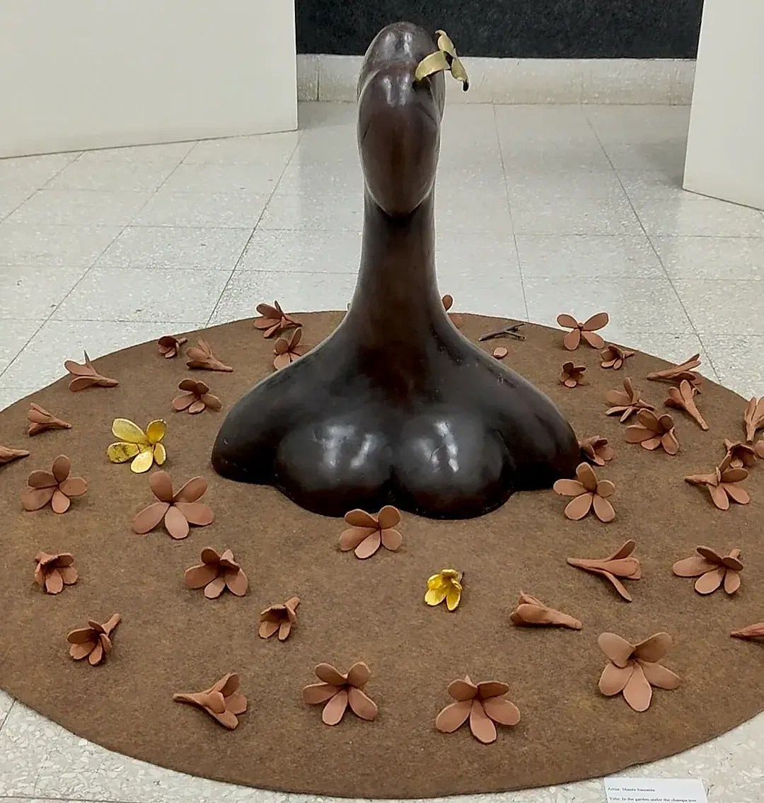 In My Garden… Under the Champa Tree, front view — the bronze bust seen from the front amid scattered ceramic petals