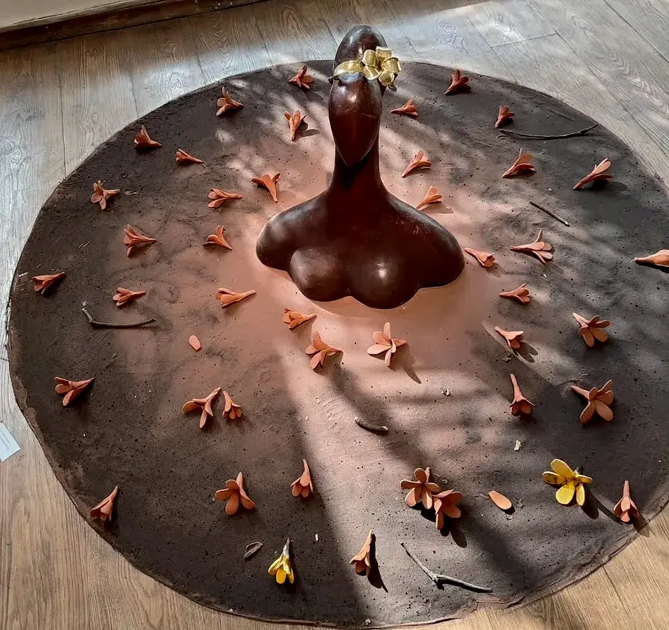 In My Garden… Under the Champa Tree — a rounded abstract bronze bust at the centre of a round terracotta disc scattered with ceramic flower petals