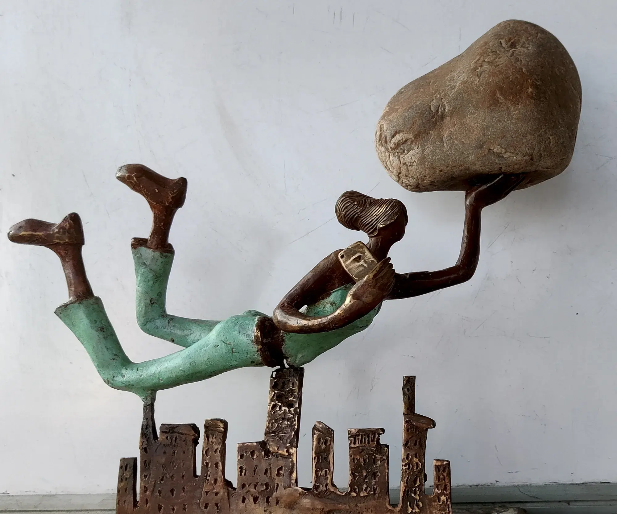 Sanjeevani — a bronze figure flying over a cityscape, a stone balanced in one hand and a mobile phone in the other