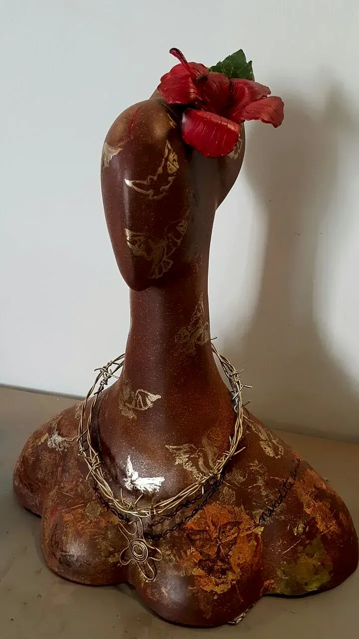 Shackled — a bronze bust adorned with a flower, wearing a barbed-wire necklace in place of a diamond pendant