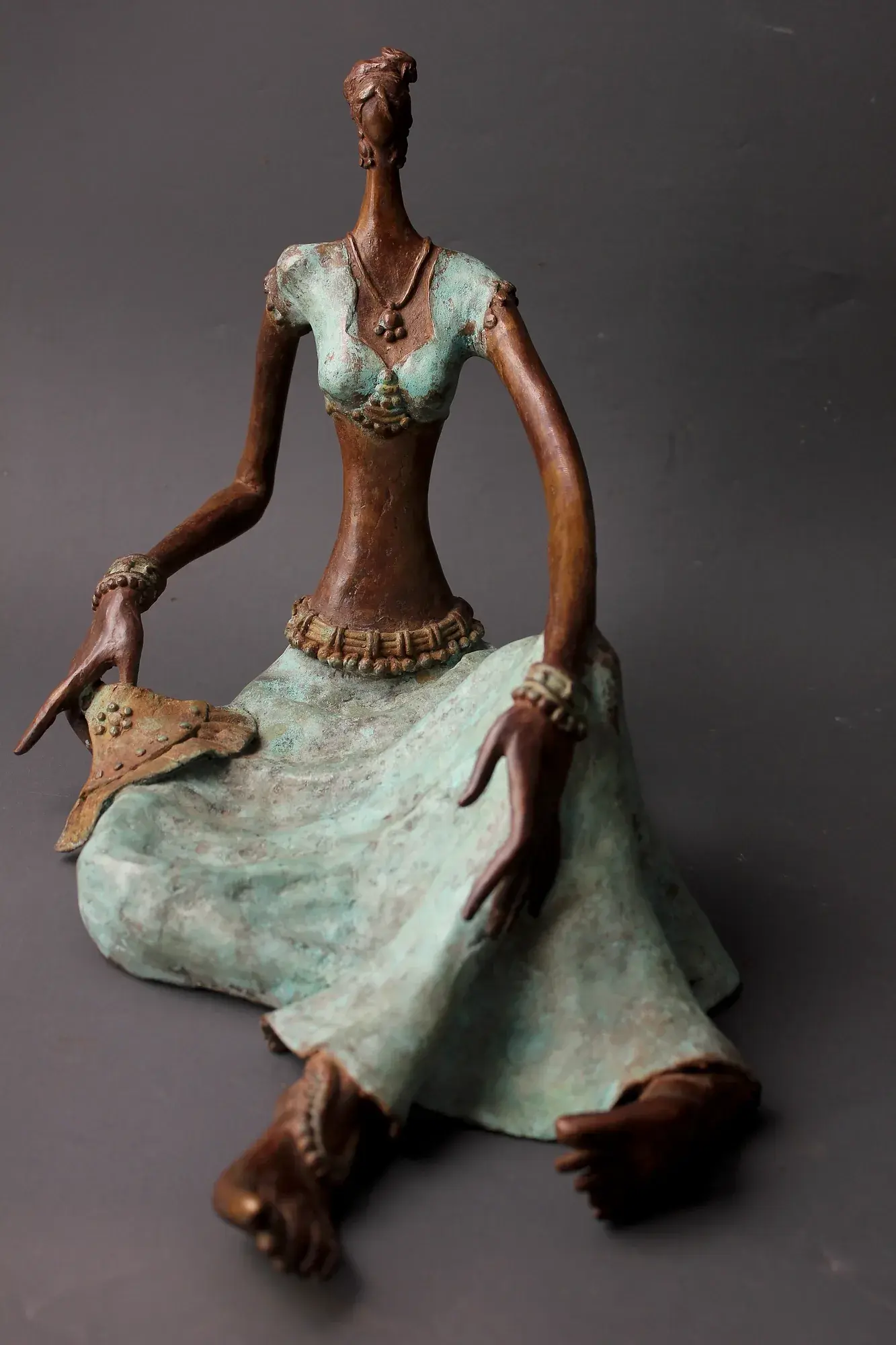 Bronze seated figure with flowers in upswept hair, legs extended, a hand-fan (punkha) raised near the face