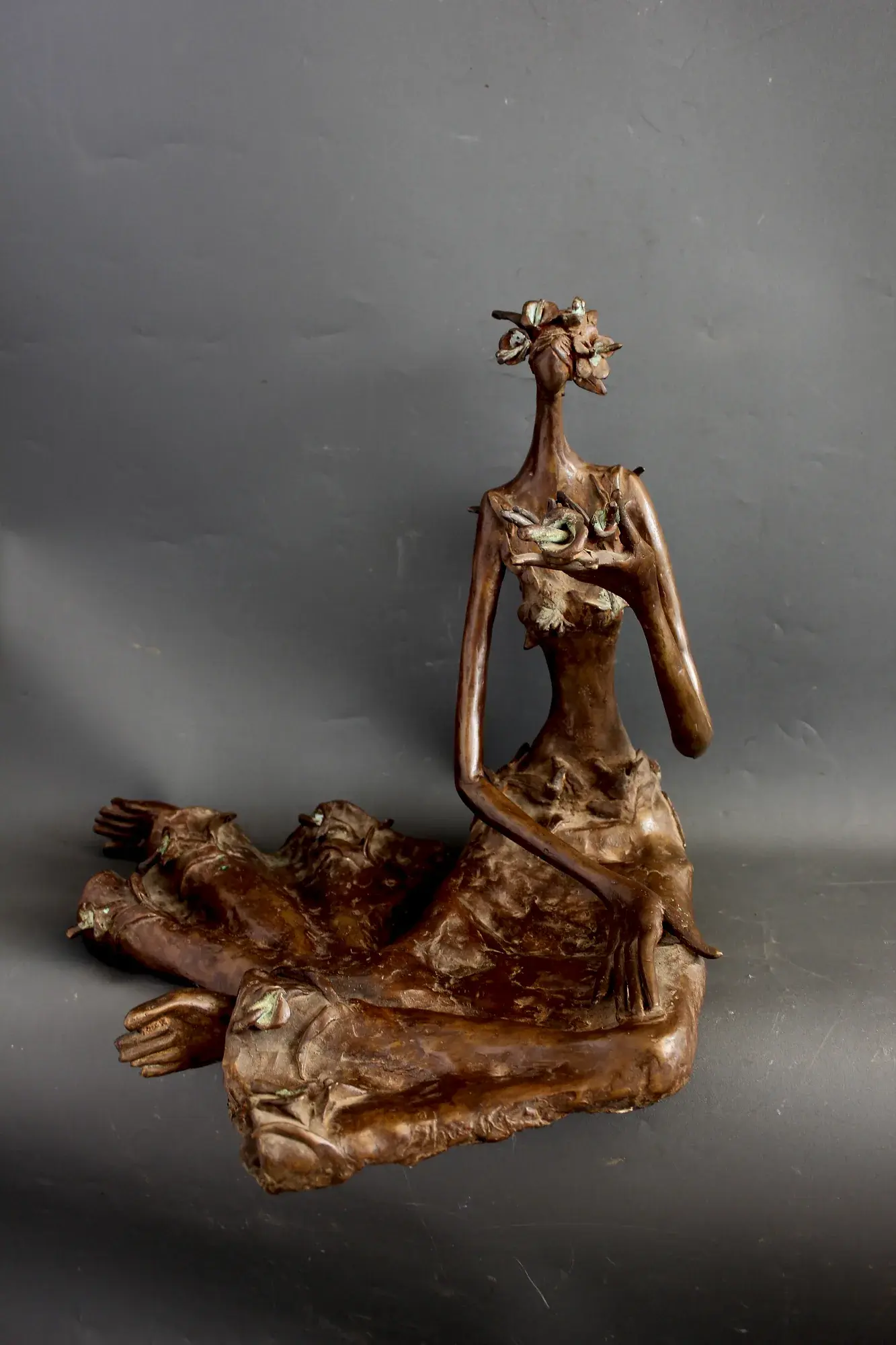 Bronze seated figure with floral appliqué on the bodice, arms crossed overhead in an oval loop