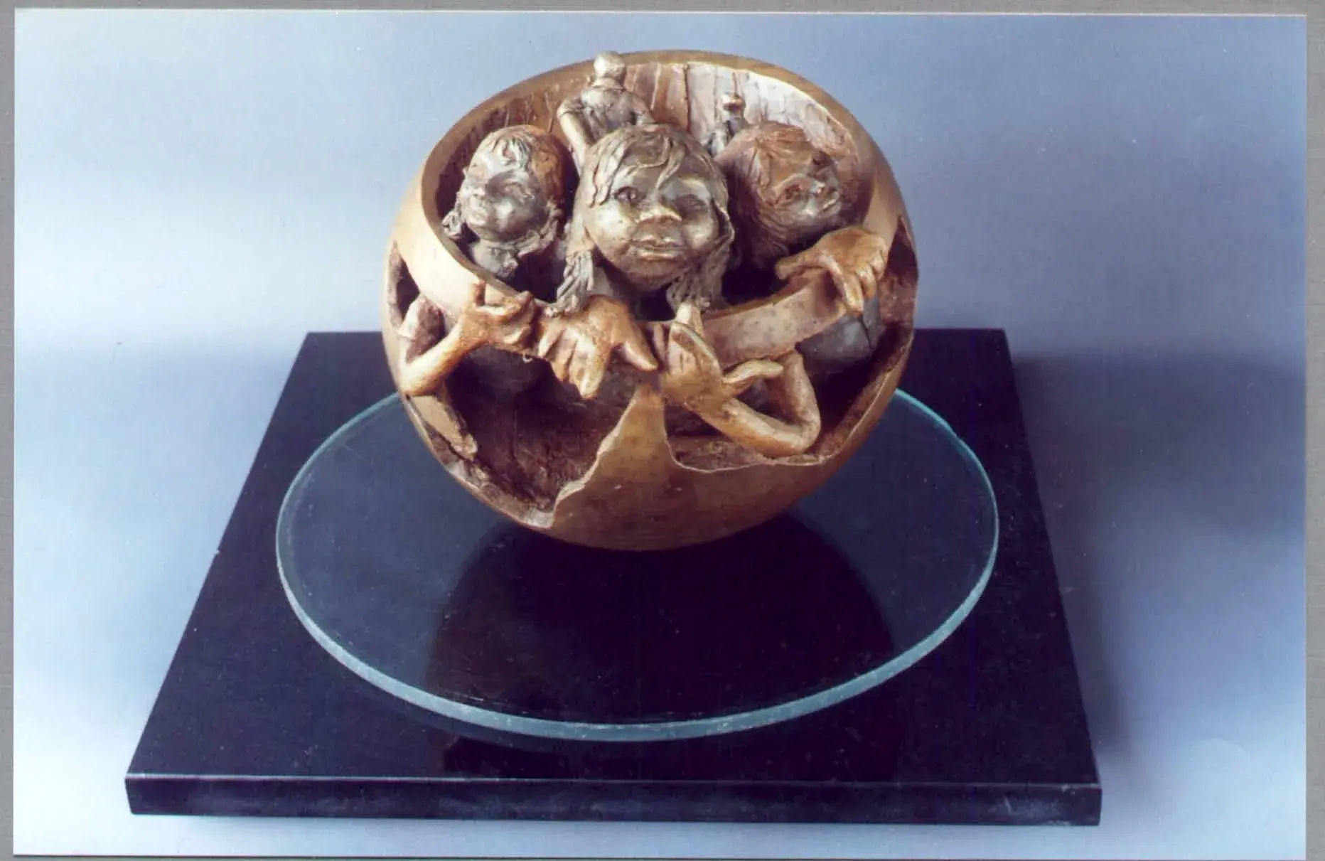 A Page From Our Family Album — three children's heads and arms emerging from a cracked bronze egg