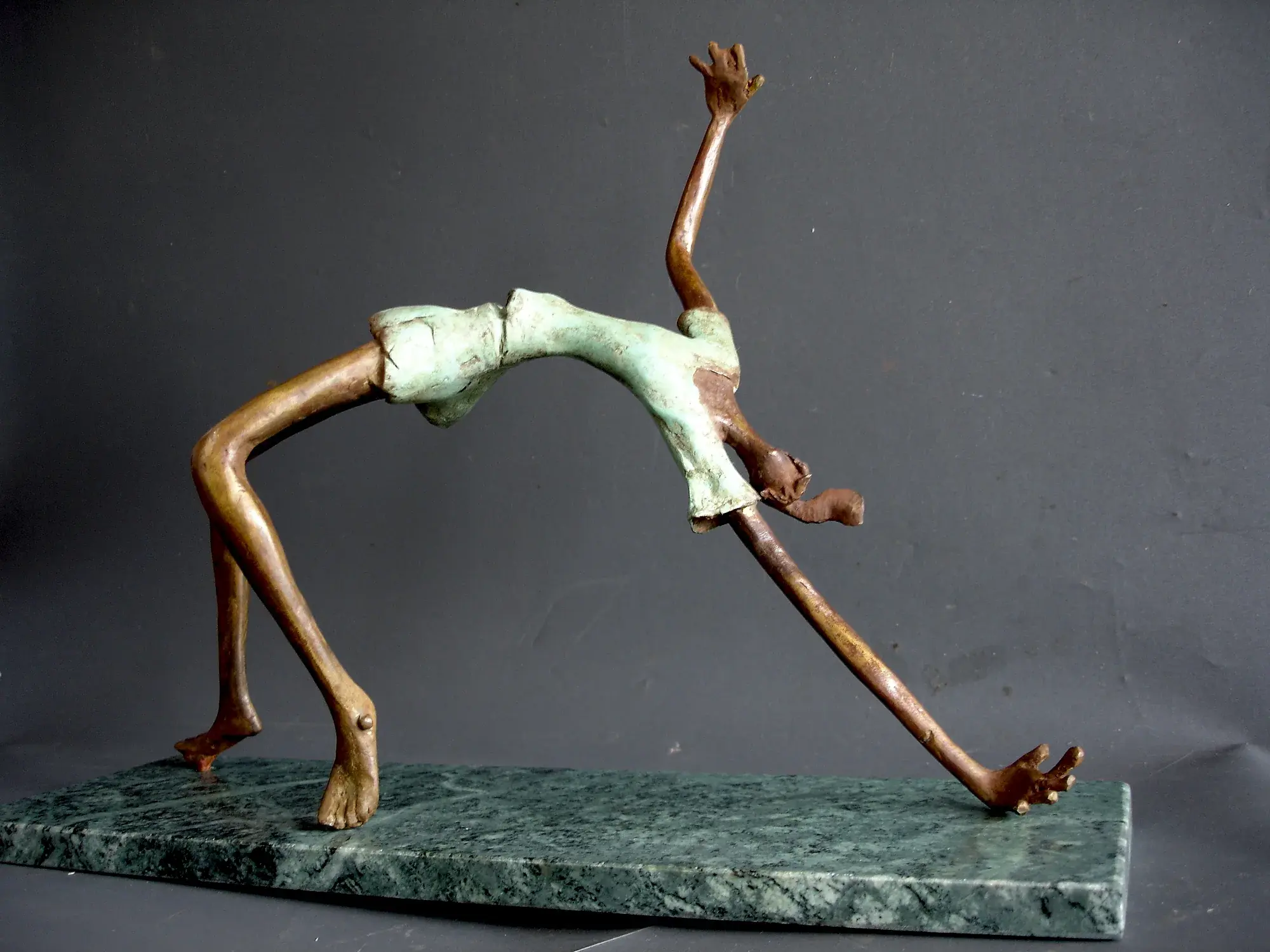 Bronze acrobat figure arched into a full backbend loop, mounted on a green marble slab