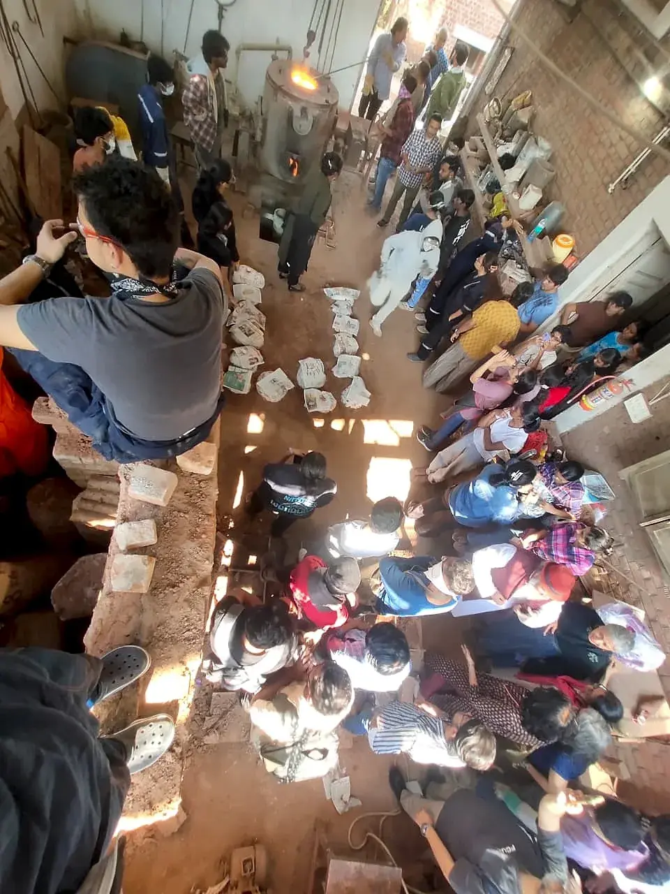 Overhead view of the foundry courtyard during the casting demonstration, with students gathered around the furnace