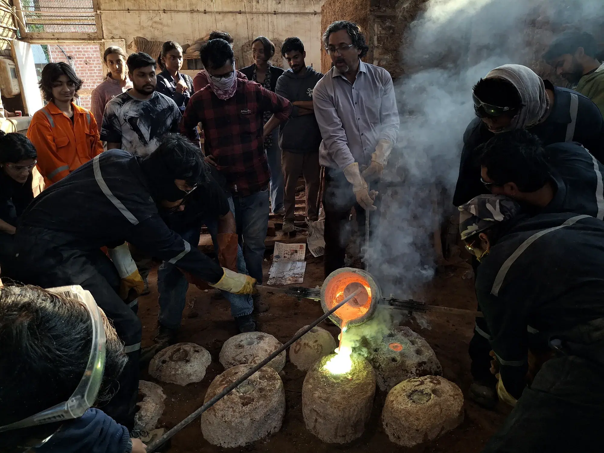 Students and faculty gathered around a crucible, pouring molten metal into moulds during a casting demonstration